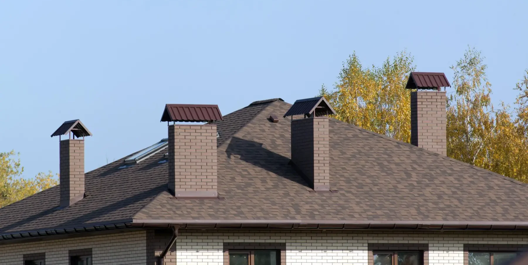 house roof with brown shingles and four ventilation pipes or chimneys